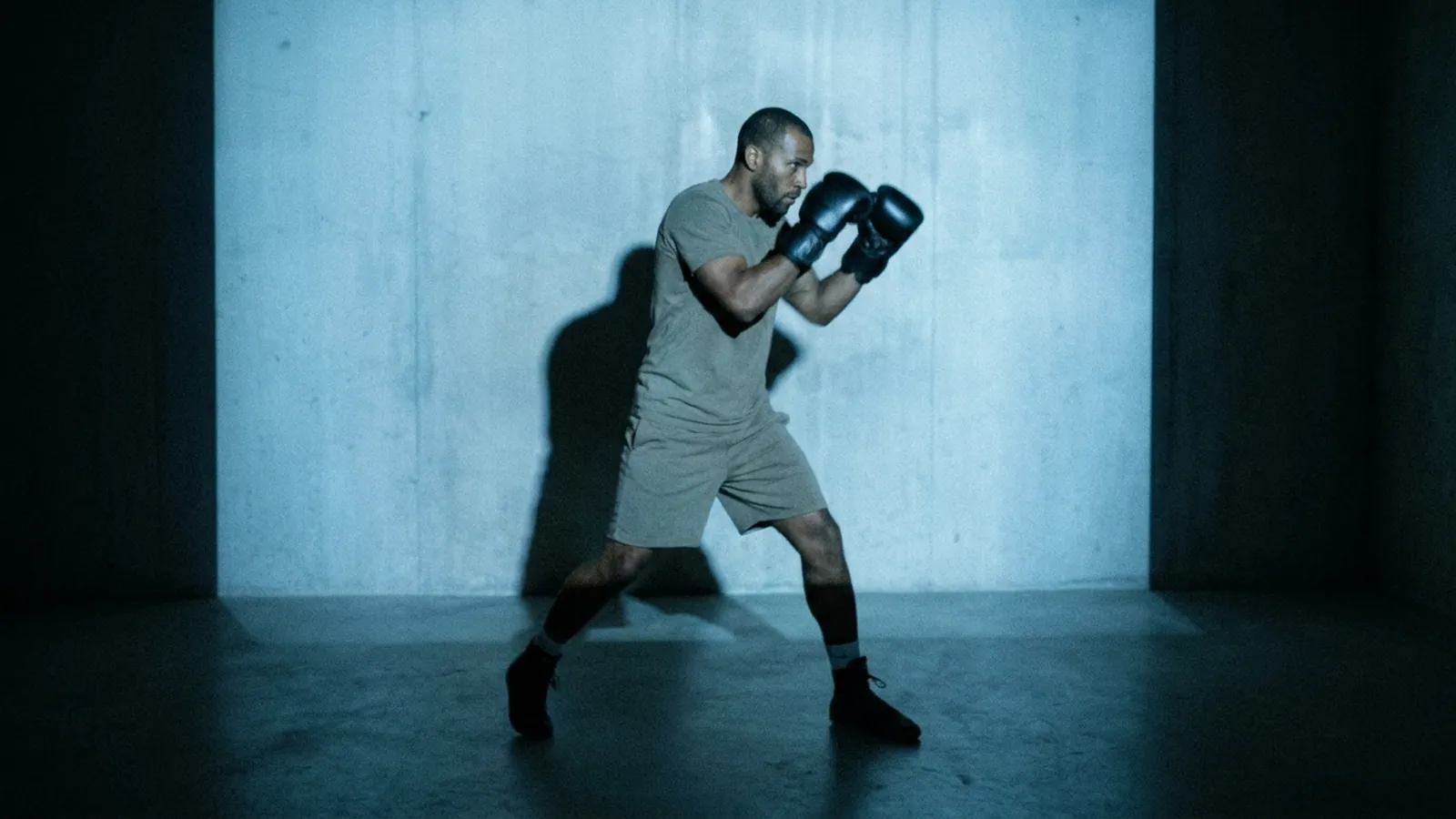 A boxer shadowboxes in front of a projected fighting game menu in a dark room