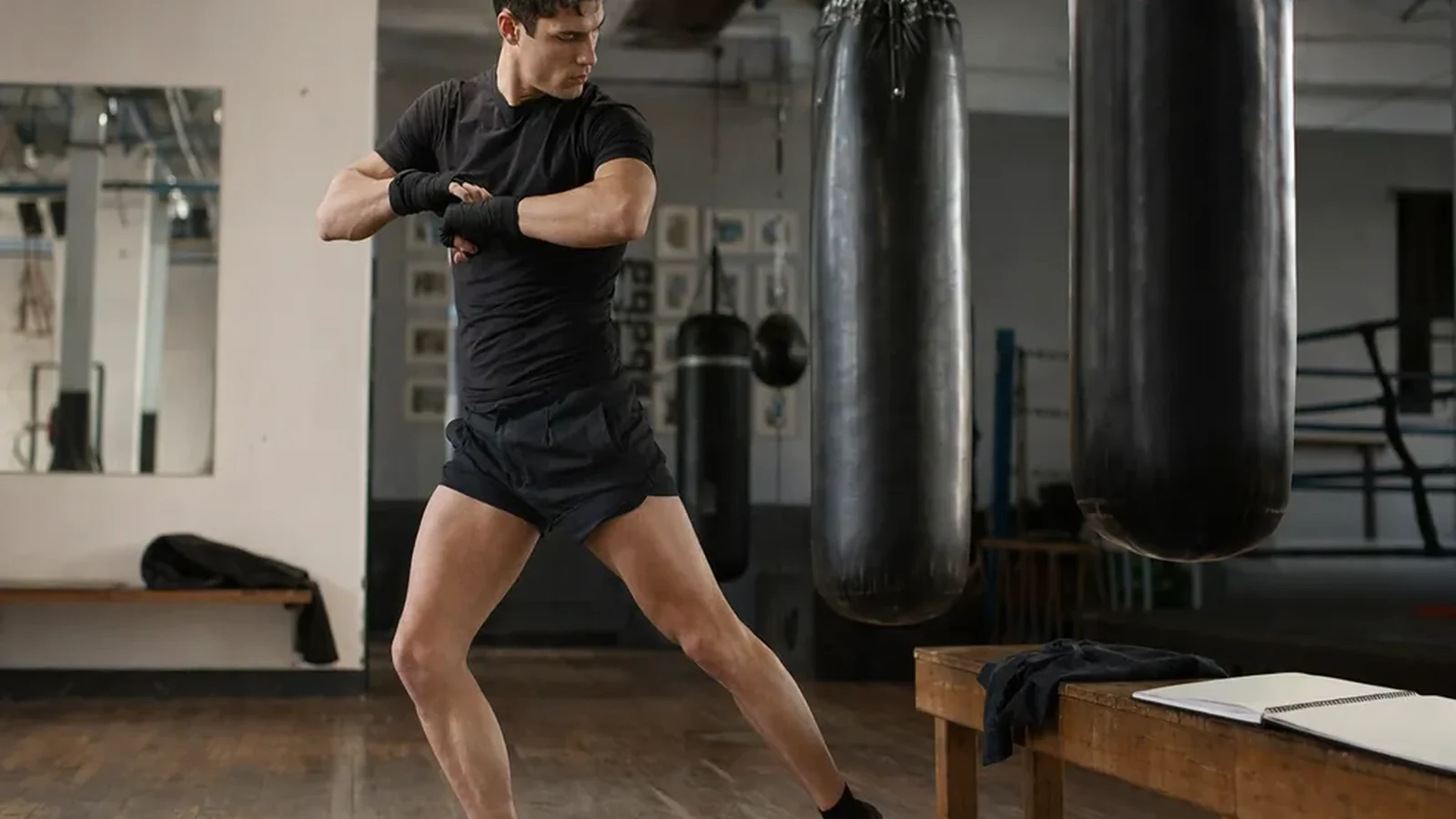 Performer wrapping hands beside heavy bags before a boxing class