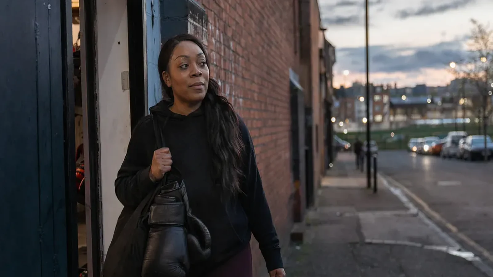 Care worker leaving a boxing gym at dusk with gloves and a plain work bag