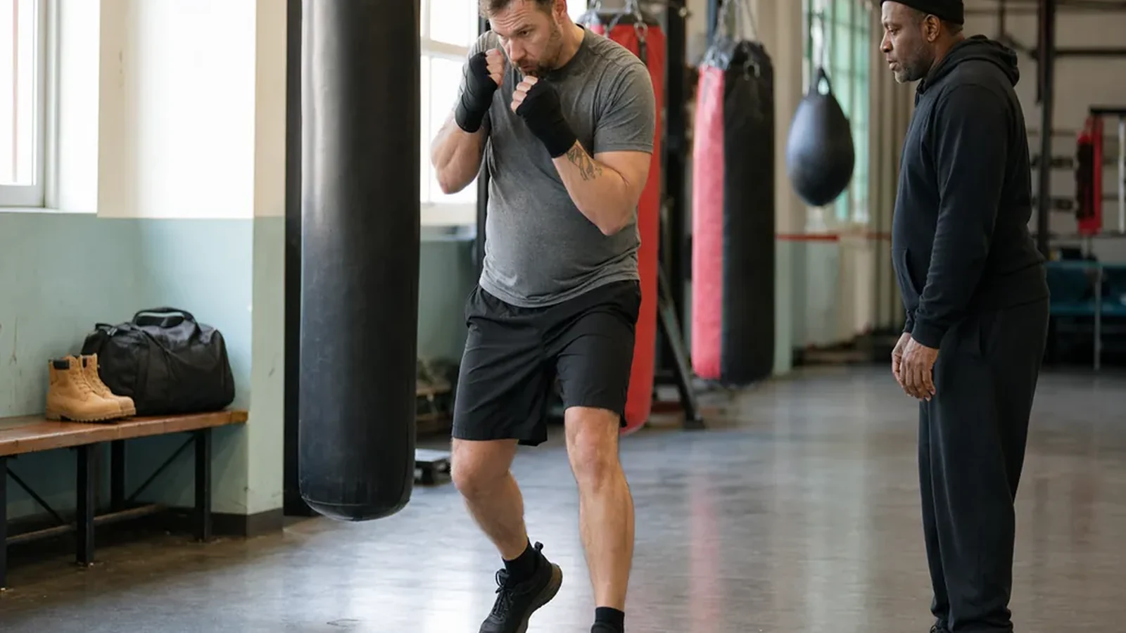 Adult beginner practising boxing footwork with a coach in a gym