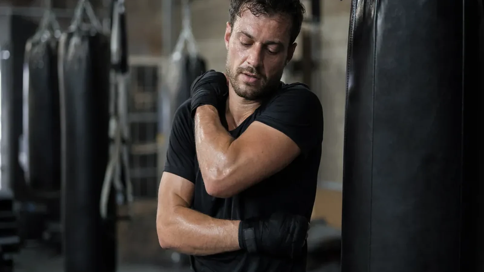 Chef in dark training kit loosening tight shoulders beside heavy bags after a long shift