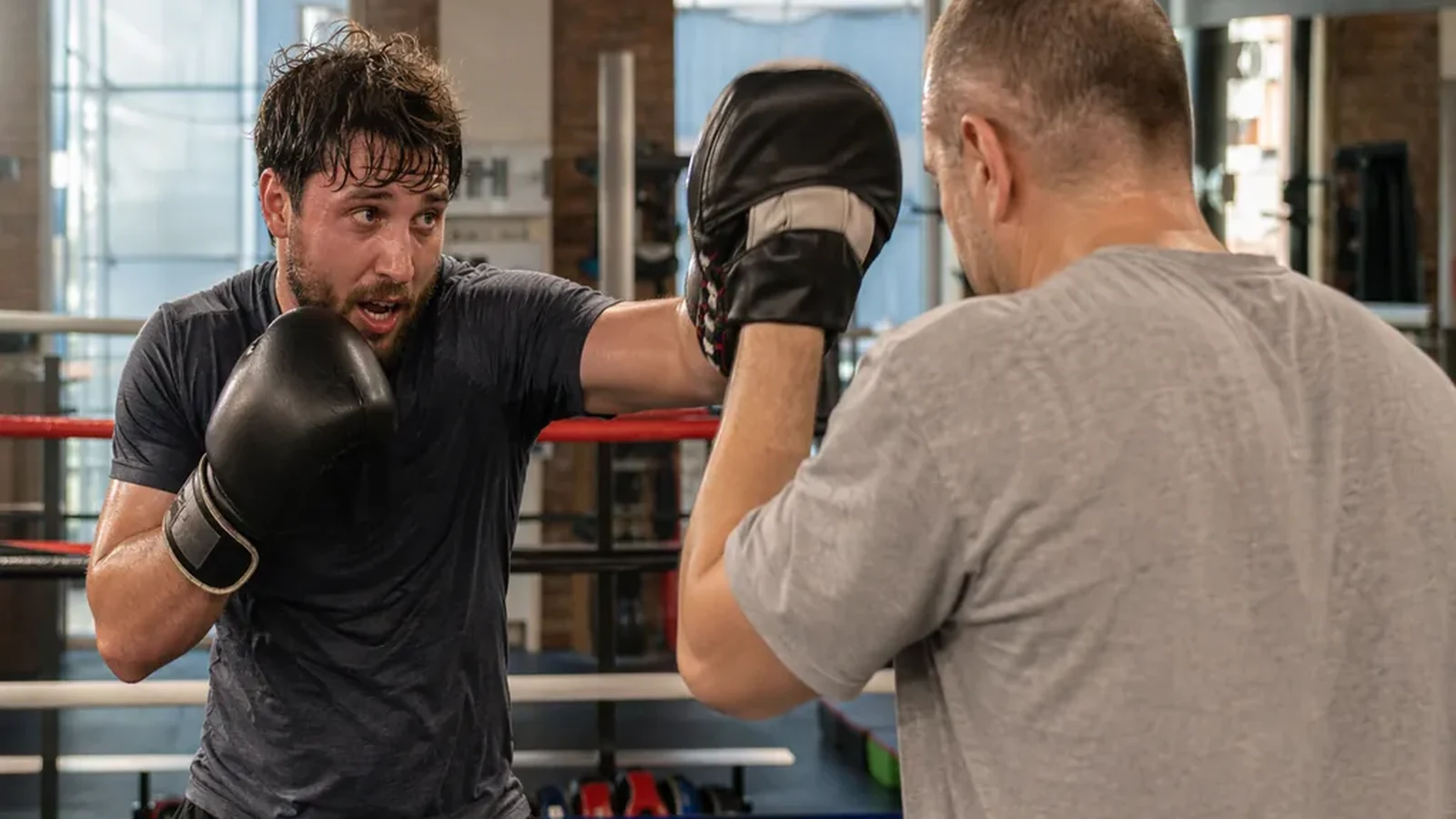Adult beginner boxer working pads with a coach inside a boxing ring