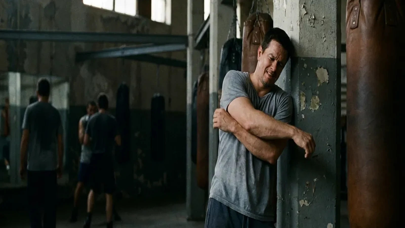 Man easing a sore shoulder beside heavy bags before evening boxing training