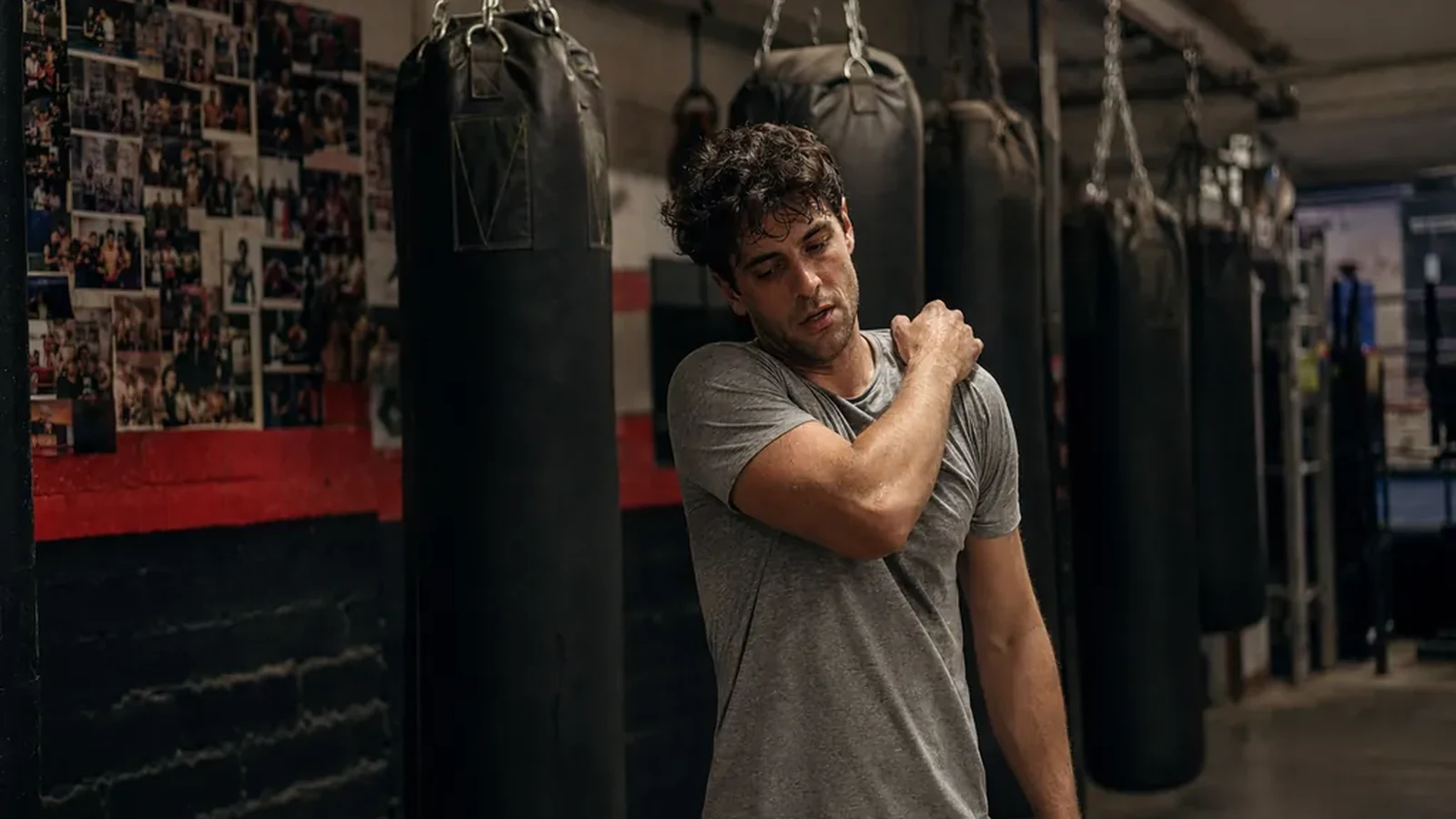 Man rubbing a sore shoulder beside heavy bags after boxing training