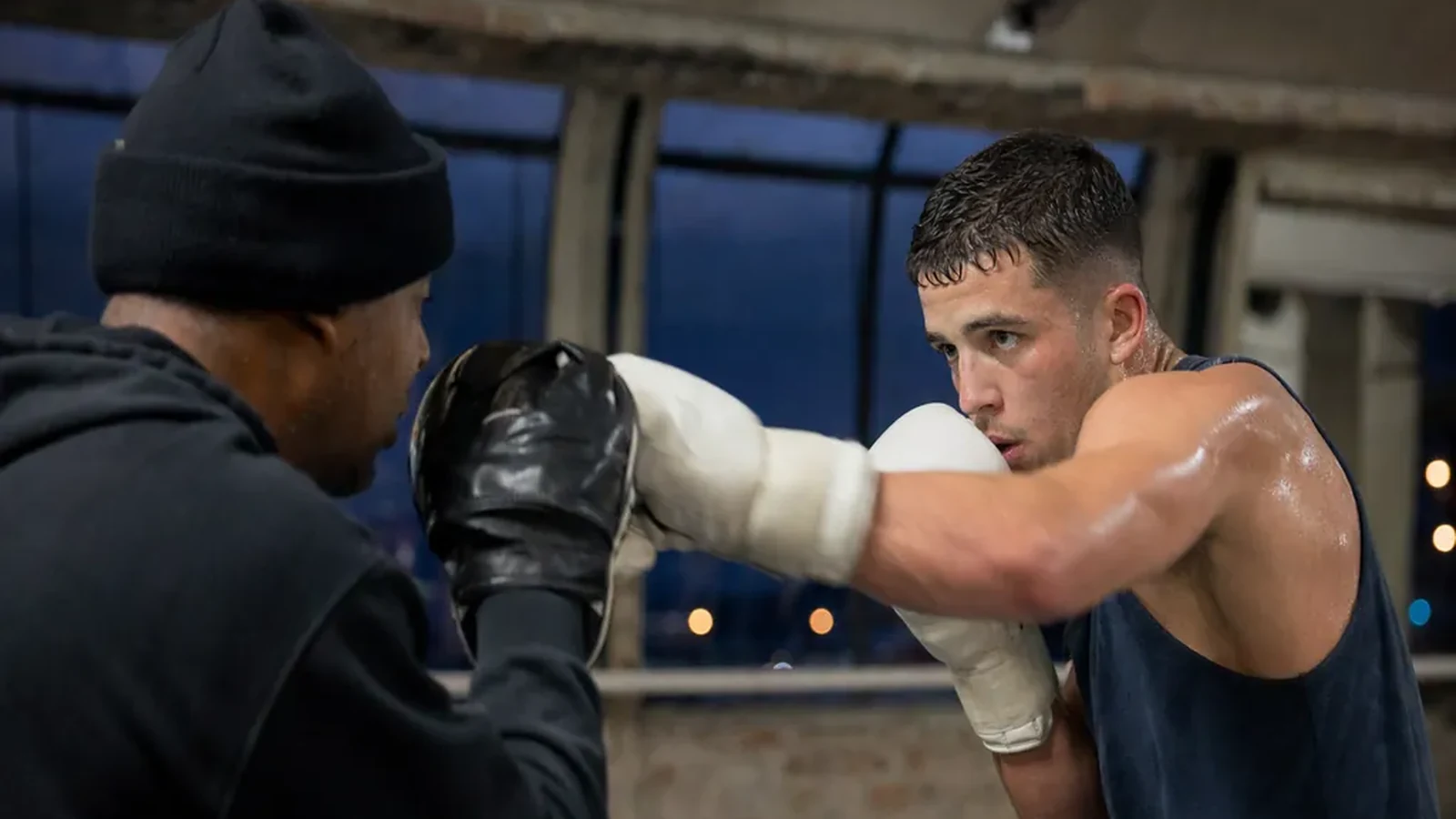 Boxer in a dark sleeveless top working pads with a coach during evening training