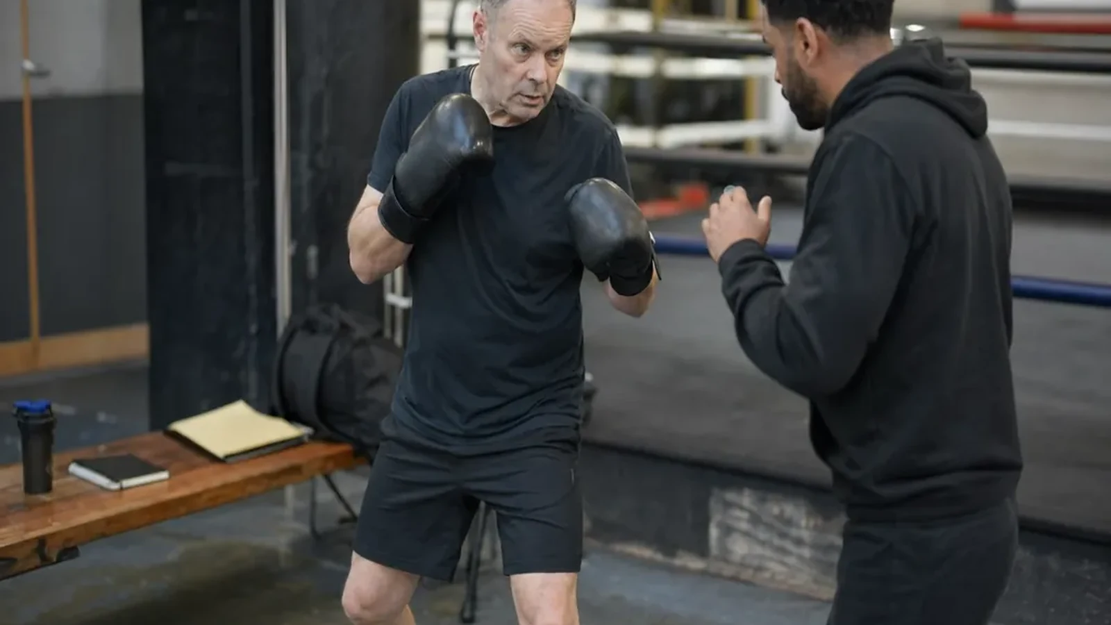 Adult beginner practising boxing footwork with a coach in a gym