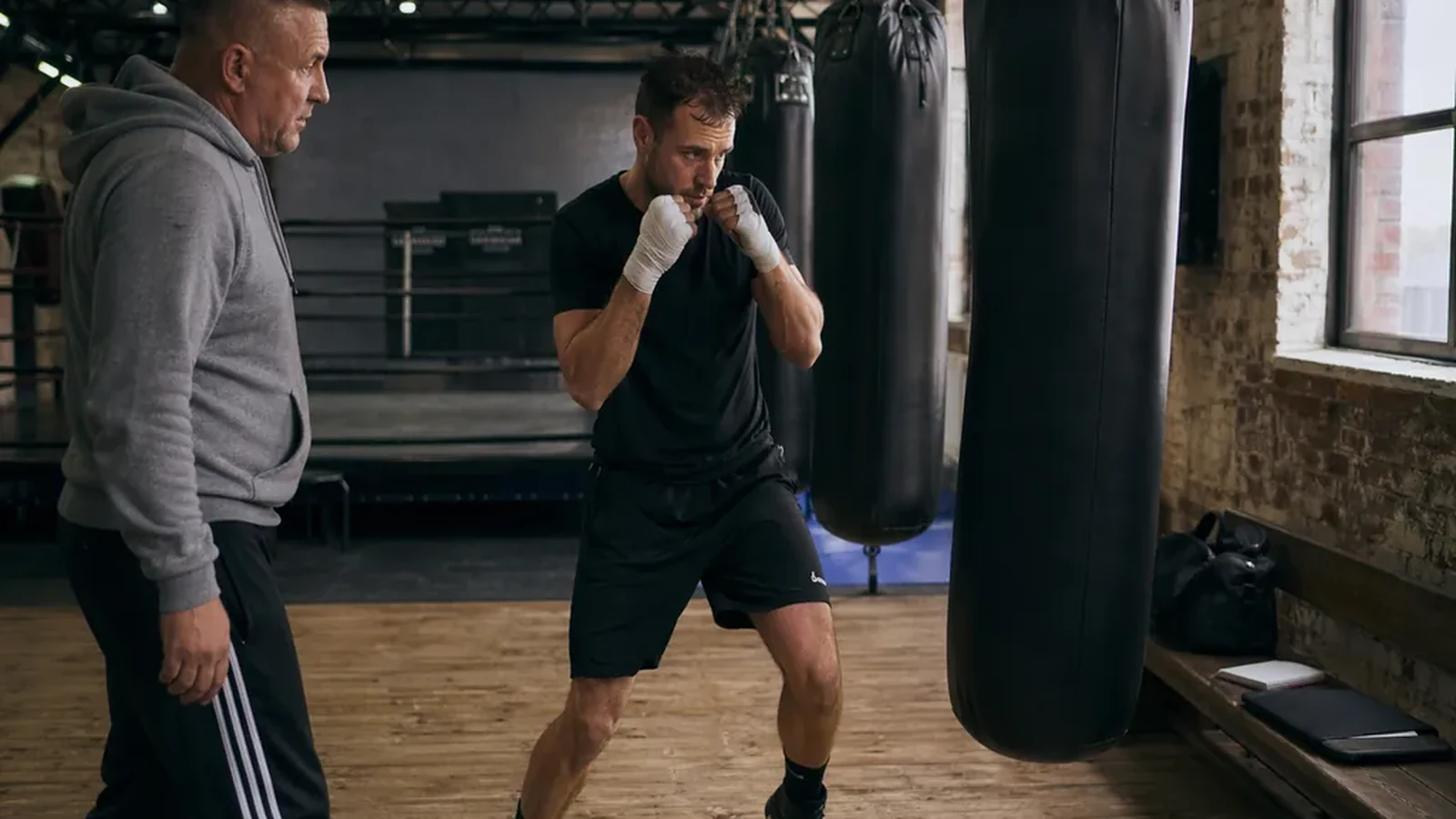 Adult beginner practising boxing footwork with a coach in a gym
