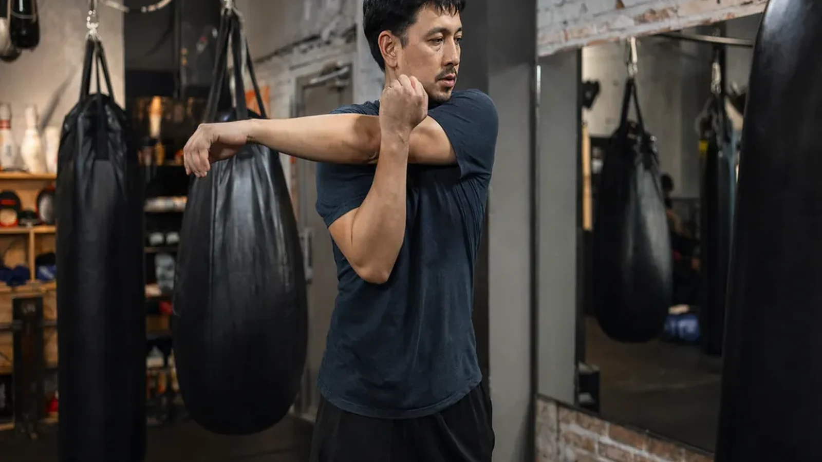 Beginner boxer stretching shoulders beside heavy bags before evening training