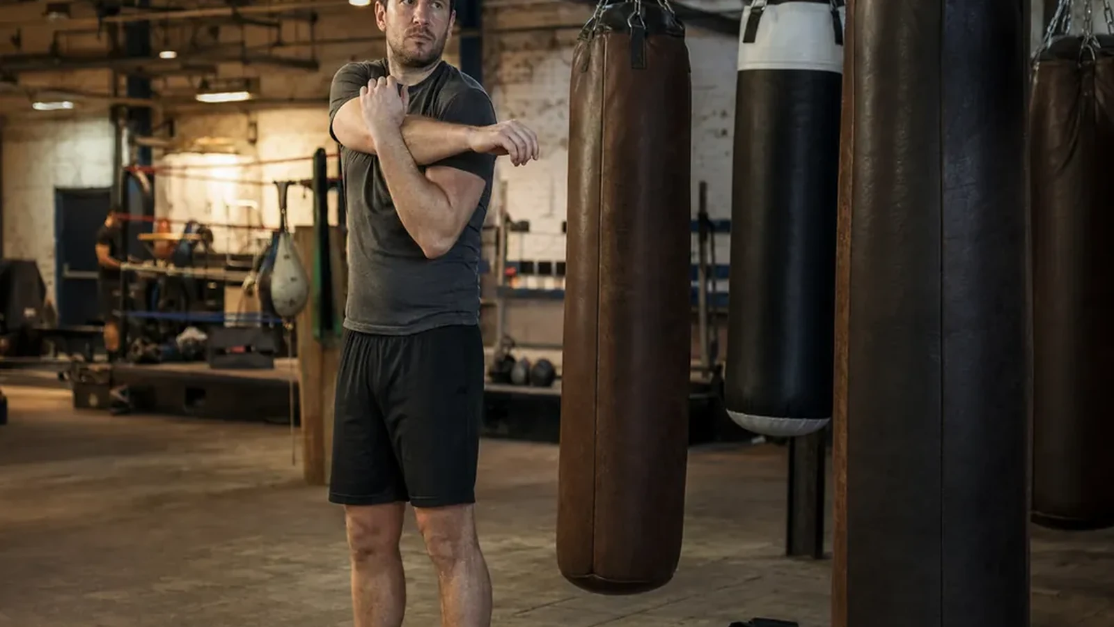 Adult boxer loosening shoulders beside a kit bag before evening training