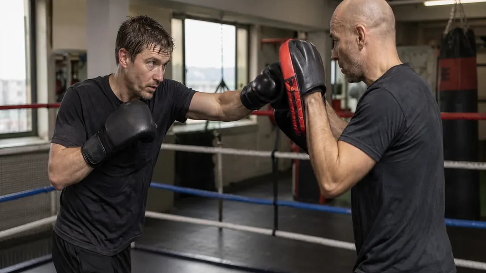 Adult beginner doing controlled pad work with a coach in a boxing gym