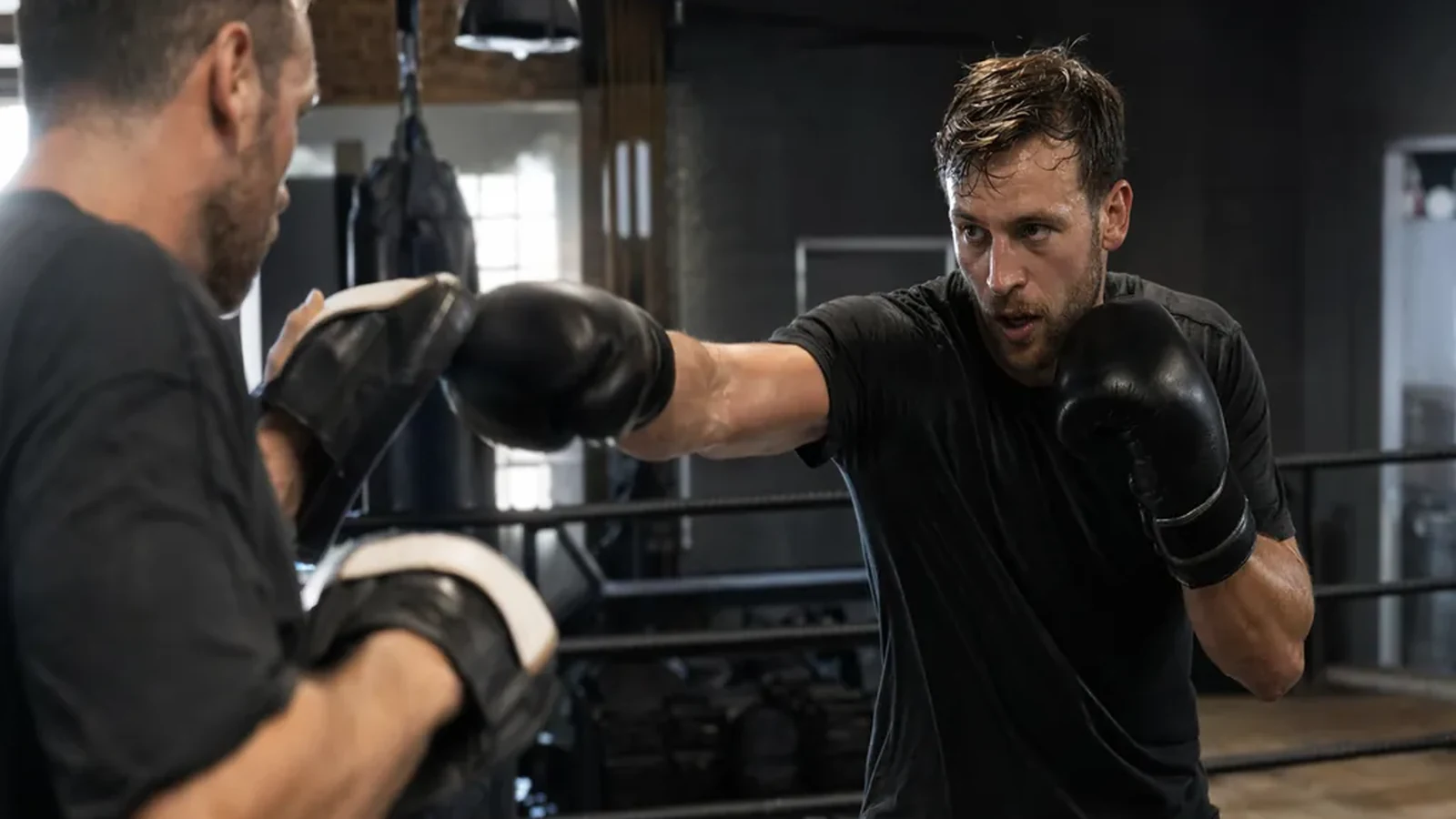 Boxer in smart black training kit working pads with a coach after an office day