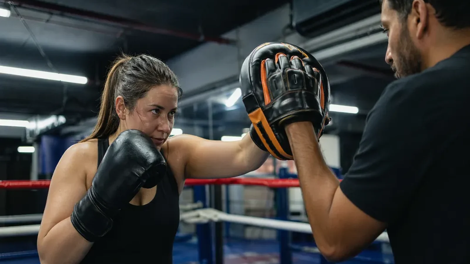 Adult beginner boxer working pads with a coach in a boxing ring