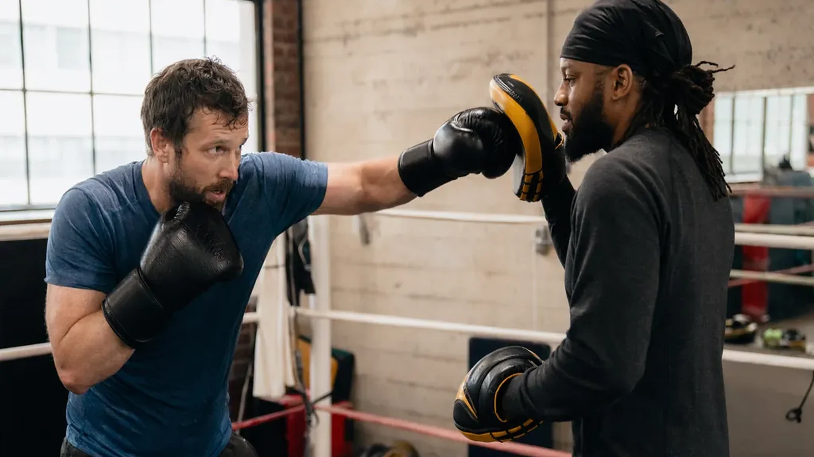 Adult beginner boxer working pads with a coach inside a boxing ring
