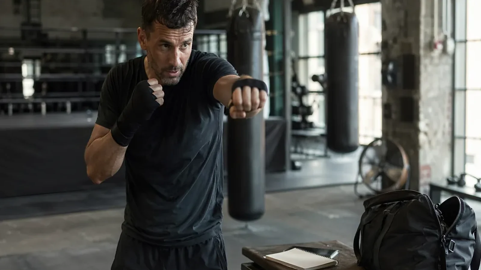 Recruiter wrapping hands beside heavy bags before a boxing class