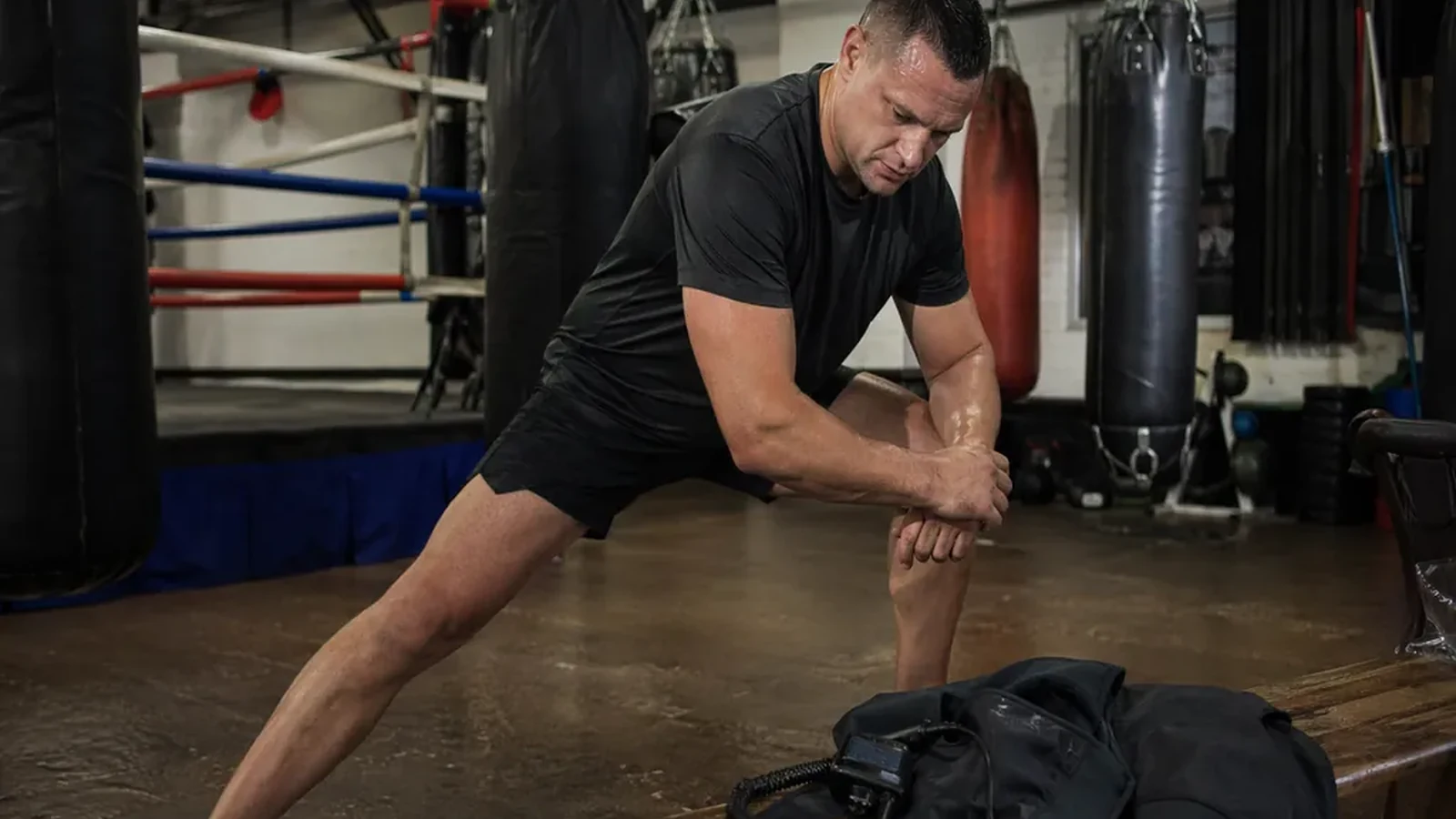 Security worker in dark training kit wrapping hands beside heavy bags before boxing training