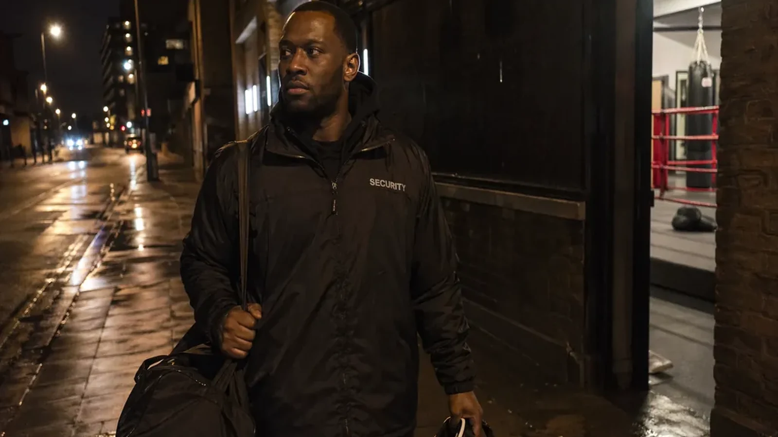 Security worker leaving a boxing gym after training with gloves and a kit bag at night