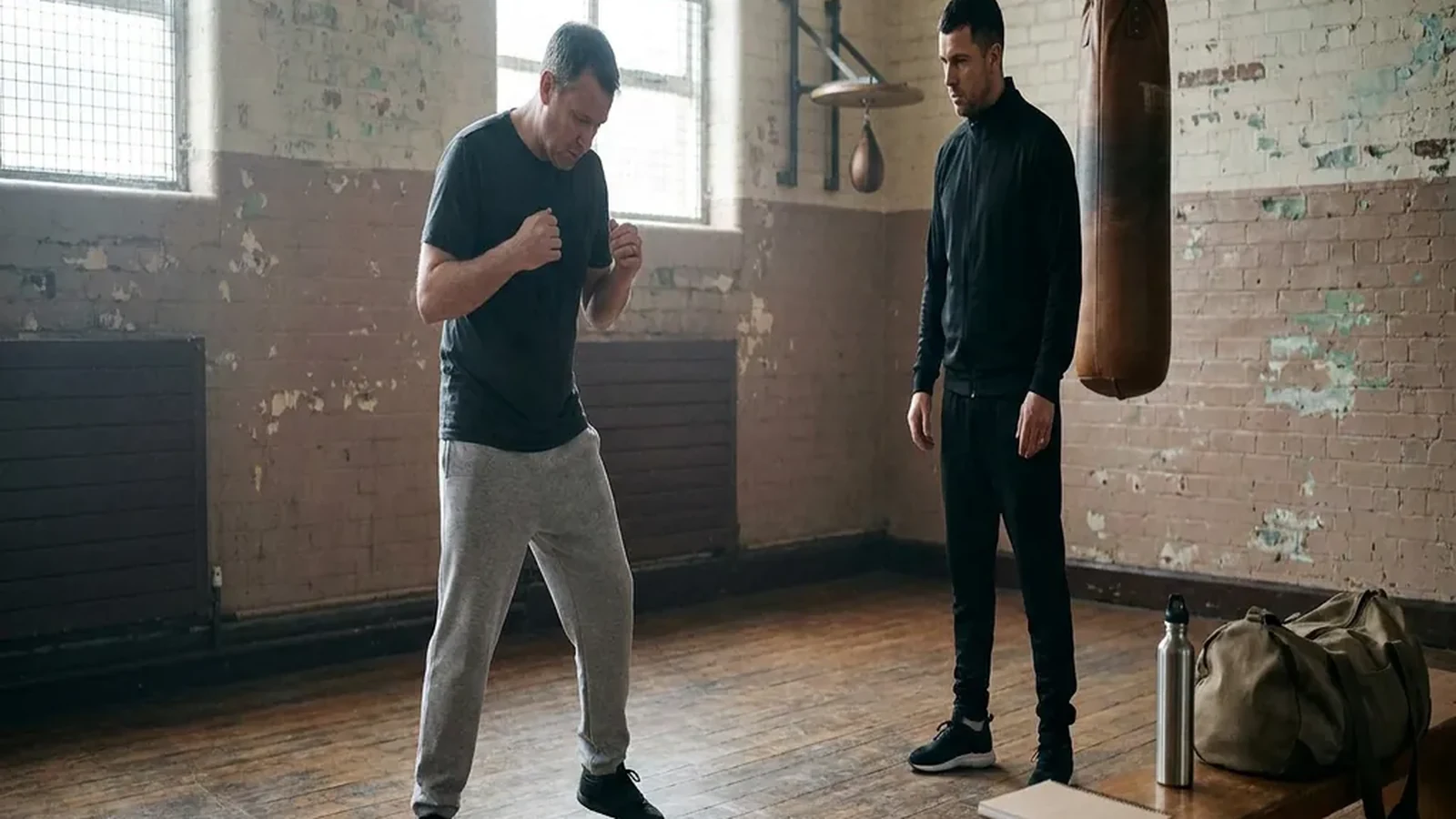 Adult beginner practising boxing footwork with a coach in a gym