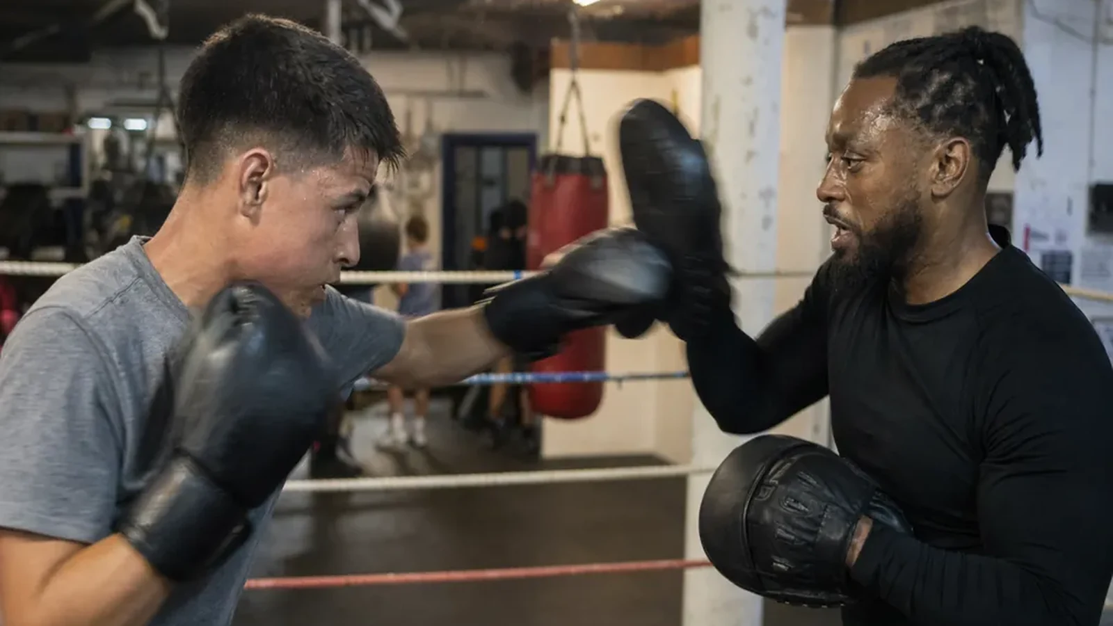 Student working controlled pad combinations with a coach in an evening boxing class