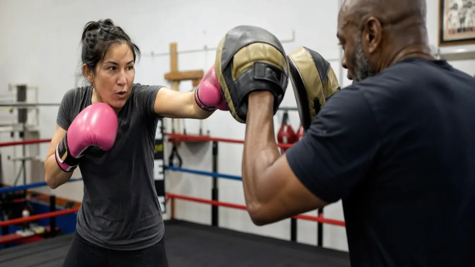 Adult beginner boxer working pads with a coach inside a boxing ring