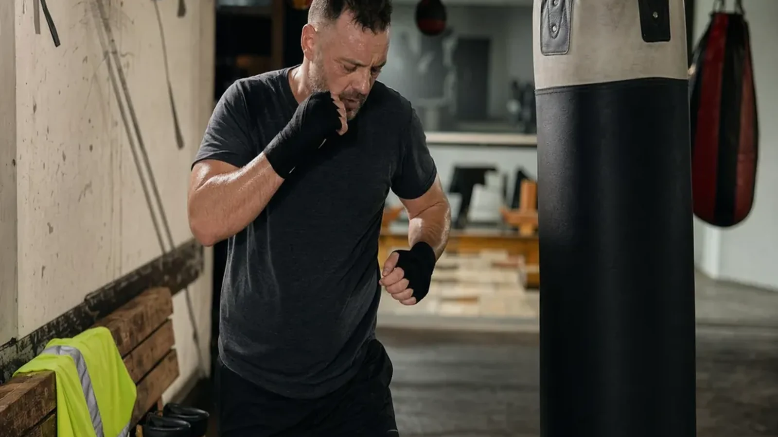Warehouse worker in dark training kit wrapping hands beside heavy bags after a shift