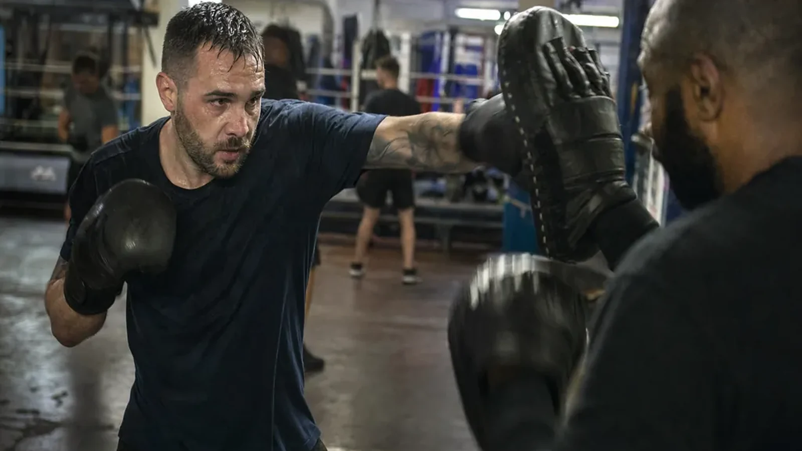 Warehouse worker doing controlled padwork with a boxing coach in an evening class