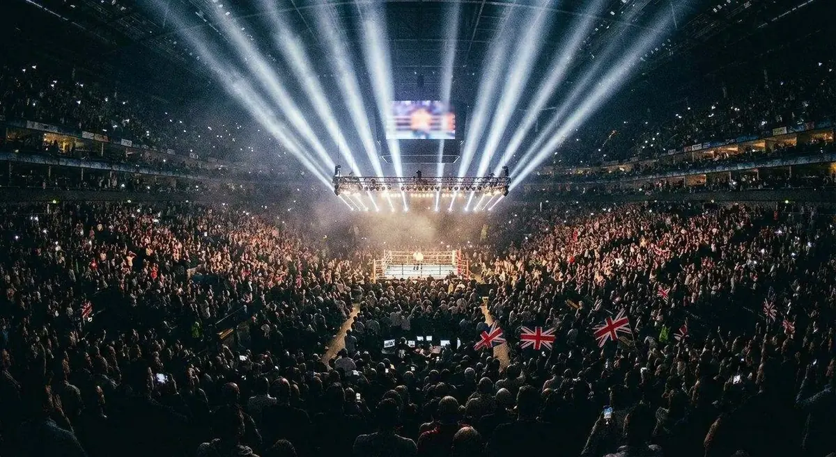 Stadium boxing arena at night with ring lights illuminating a sold out crowd