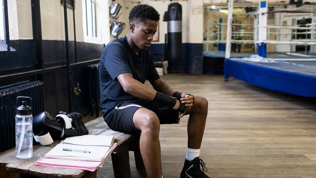 Sixth-form student preparing boxing wraps beside revision notes in a community gym