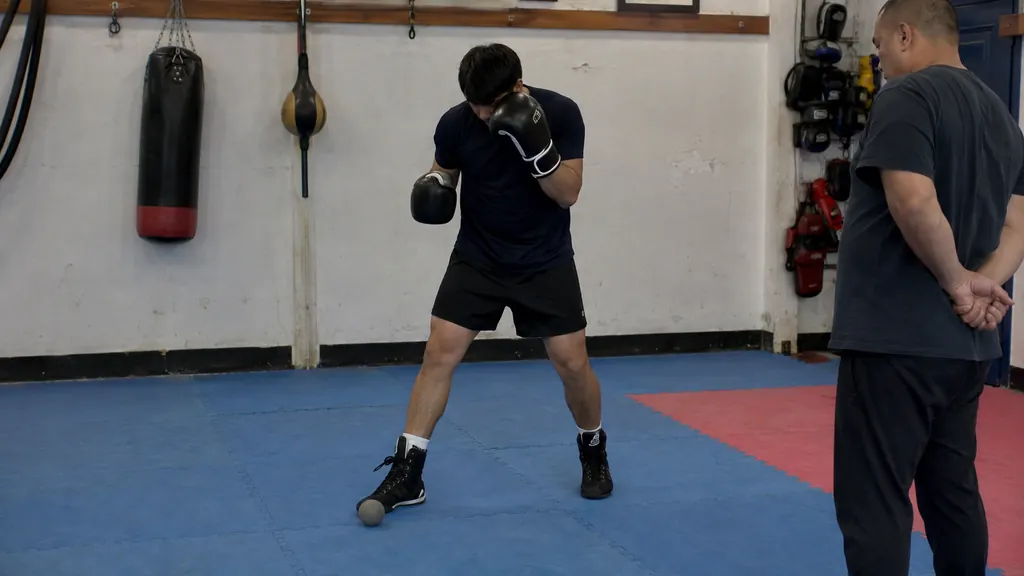 Anonymous adult boxer using a small training ball as a distance marker while keeping the rear glove high in a community boxing gym
