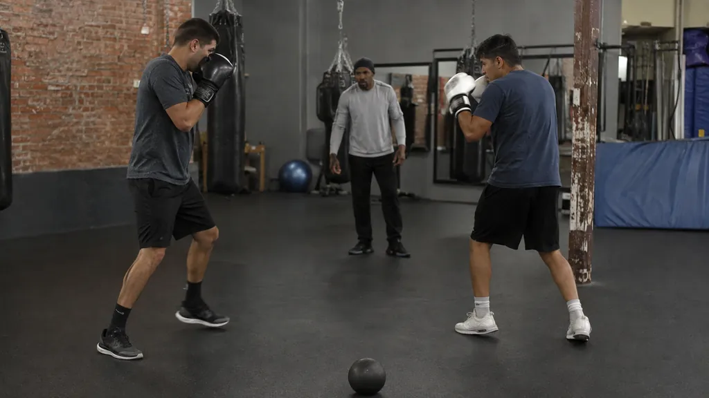 Anonymous adult boxer recovering to a balanced stance after a controlled forward step in a community boxing gym with a coach and small range marker