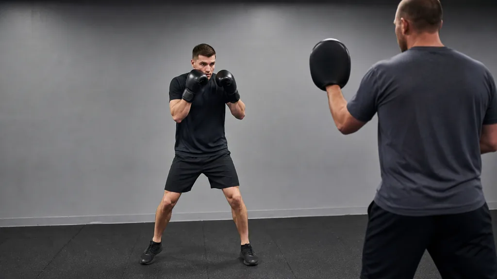 Adult boxer making a compact side step away from a coach-held focus mitt in a modest community boxing gym