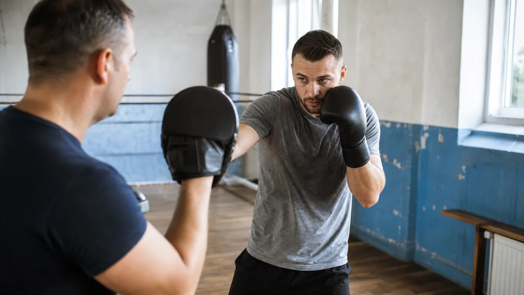 Two adult boxers doing a slow partner drill with a compact lead-hand deflection and a coach watching