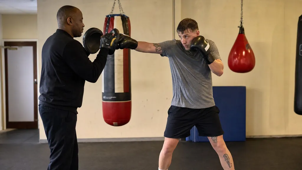 Anonymous adult boxer extending a straight lead hand after a controlled hook on focus mitts in a community boxing gym