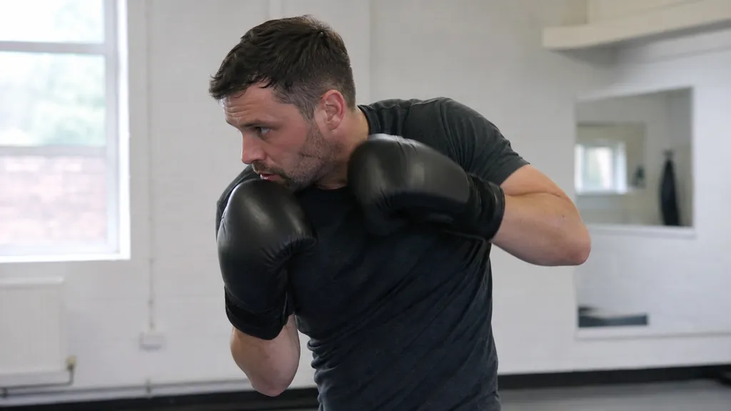 Adult boxer practising a small defensive slip with both black gloves held close and eyes forward in a bright community gym