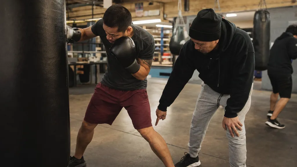Adult boxer working close to a heavy bag while a coach checks his guarded position