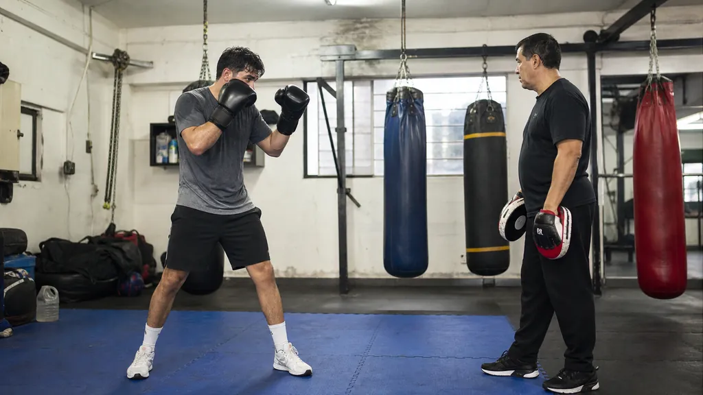 Adult boxer settled in a balanced high guard beside a coach holding focus mitts after a technical drill