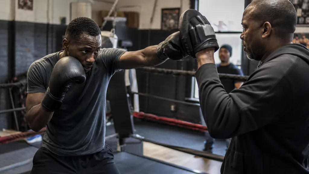 Beginner boxer practising an off-line jab with a coach holding pads nearby
