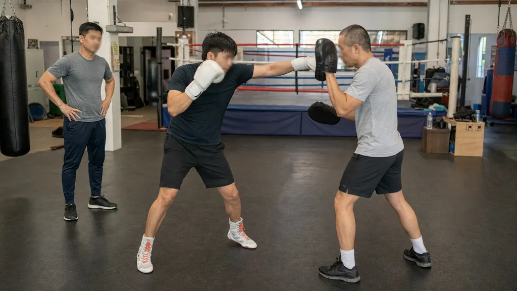 Coach supervising a slow controlled straight-punch mitt drill in a boxing gym