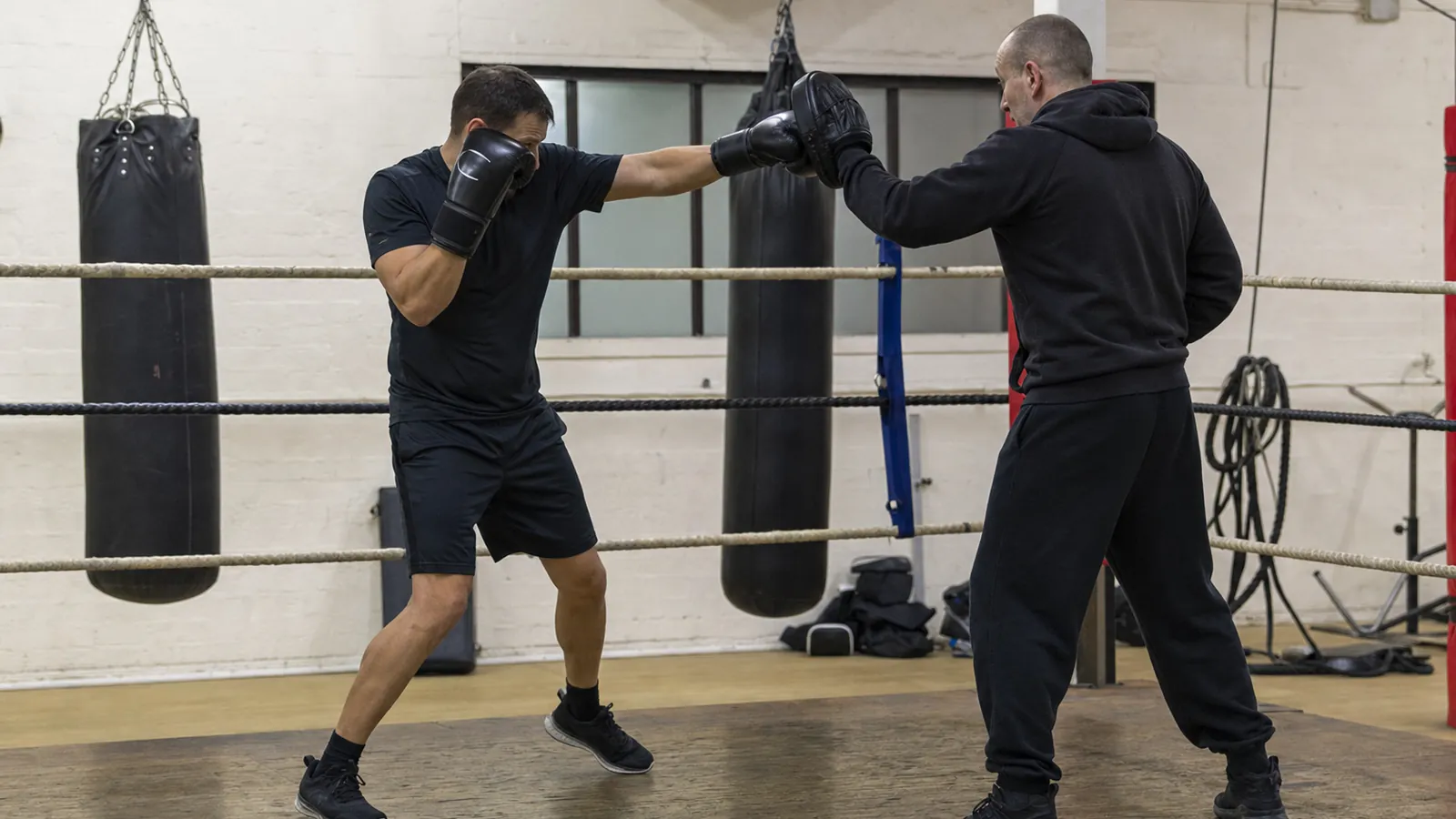 Adult boxer taking a measured lead-foot step and sending a controlled jab to a coach's mitt during a technical drill