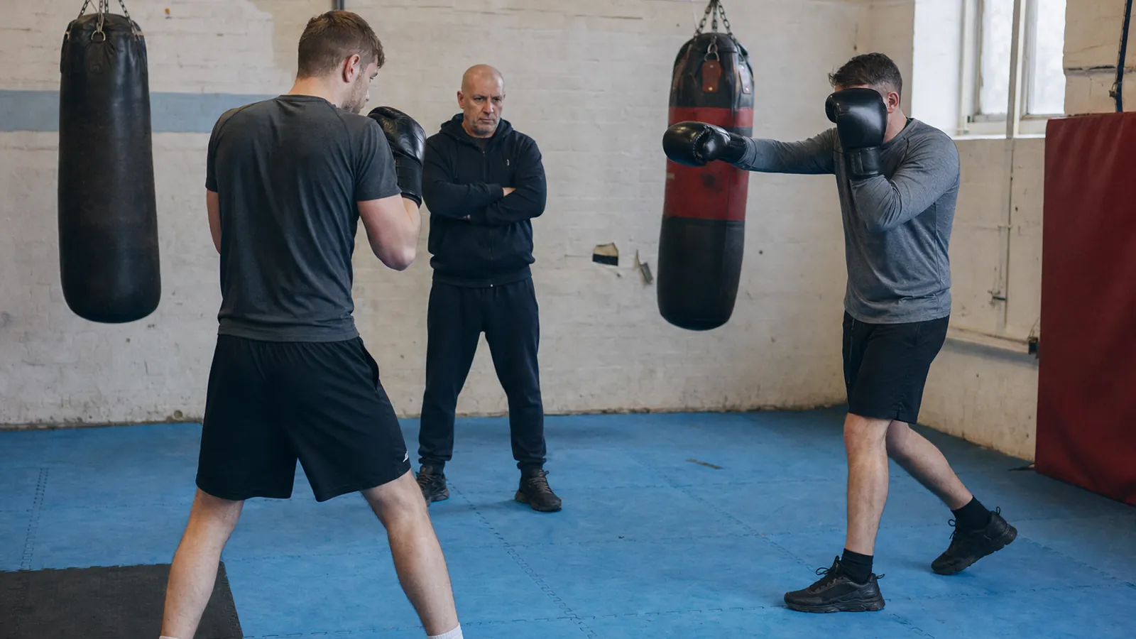 Two adult recreational boxers practising a slow glove-to-glove distance drill while a coach watches their balance
