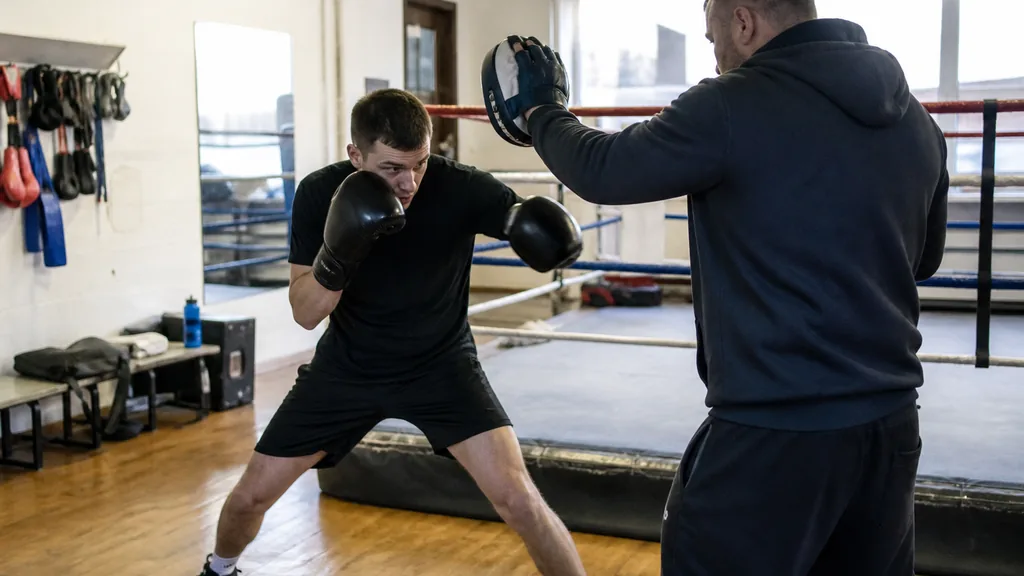 Adult boxer making a compact lead-side slip while keeping both gloves high and feet balanced in a community boxing gym
