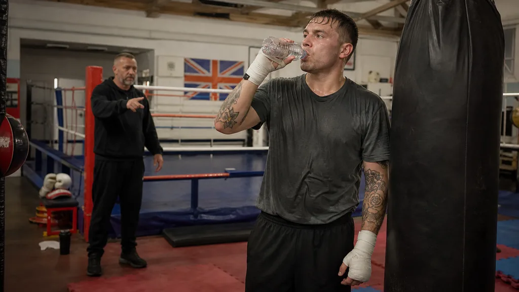 Recreational boxer takes a small water break beside a heavy bag while a coach checks in