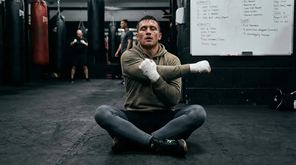 Boxer doing stretching and recovery exercises after training, sitting on gym floor breathing deeply